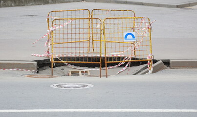 The failure of the asphalt pavement on the road is fenced with yellow metal barriers