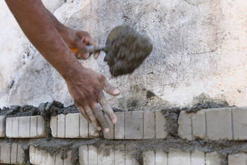 Worker plastering brick wall with putty knife at construction site