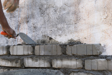 Worker with trowel plastering brick wall at construction site