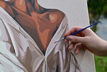 The artist is painting a picture, holding a paintbrush in hand.

