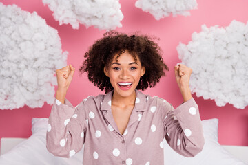 Photo of impressed lucky lady wear pajama rising fists enjoying soft clouds isolated pink color background