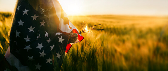 Young woman holding bengal fire with American flag at sunset.America celebrate 4th of July....