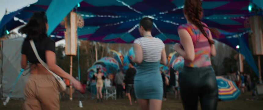 Two young women run towards festival stage at sunset