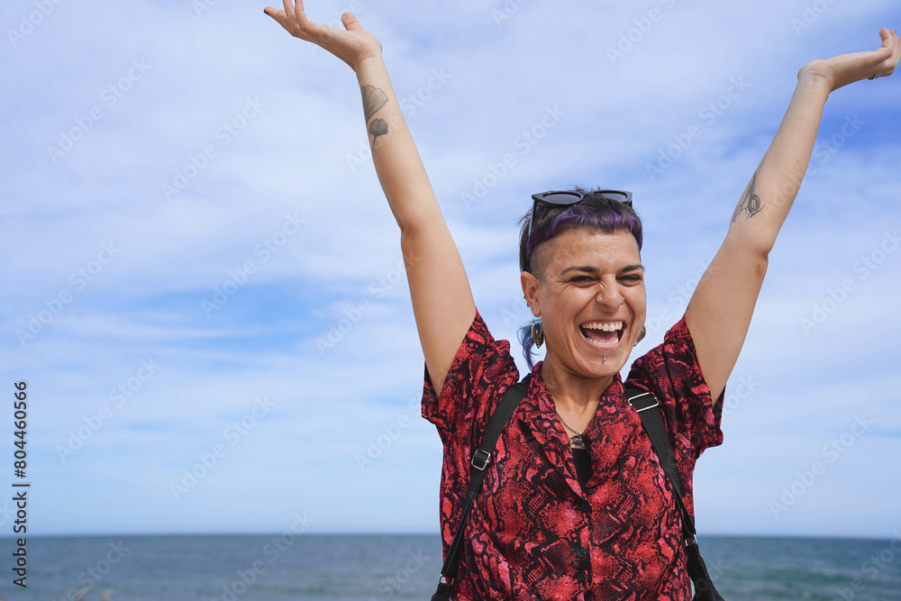 Wall mural A gay woman with purple hair is smiling and holding her arms up in the air. Concept of summertime and happiness