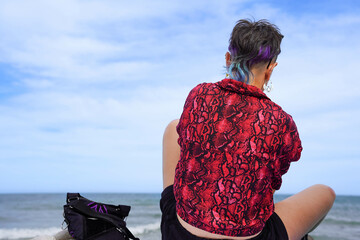 Back of alternative woman with blue hair and a red and black snake print shirt looking at the...