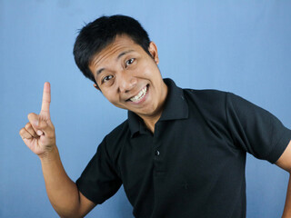 funny face expression of asian man in black shirt smiling, looking at camera while pointing up.