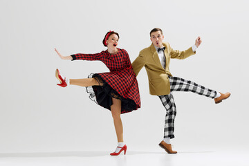 Young man in checkered trousers and mustard jacket dancing with woman dressed in red dress isolated over white studio background. Concept of art, retro and vintage, hobby, entertainment, 20s