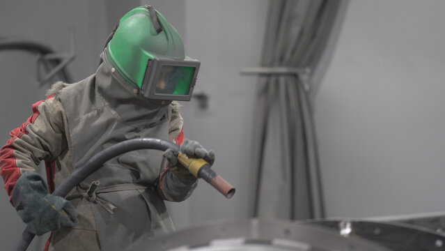 Masked worker is sandblasting or painting the product.

