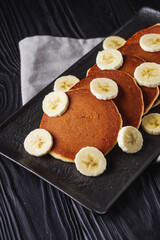 fresh tasty pancakes with banana and condensed milk on a black rustic background