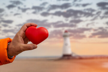red heart in hand against lighthouse. Fall in love with holiday at seaside concept