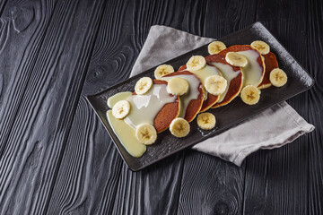 fresh tasty pancakes with banana and condensed milk on a black rustic background