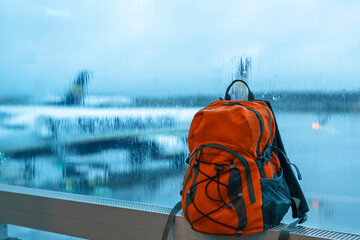 orange backpack  in airport against airplane on rainy day. Travel touristic concept. Protect...