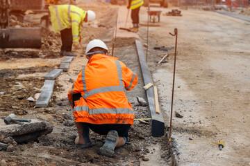 Groundworkers in hi-viz leveling concrete  kerbs on  construction site