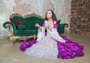 Beautiful woman in fantasy white and purple rococo style medieval dress sitting on the floor near...
