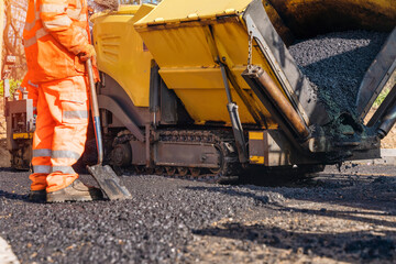 Asphalt paver with hot tarmac roadworker operator in hi-viz laying new road surface 