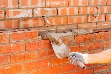 hand holding Masonry Trowel in gloves of bricklayer laying bricks on construction site 
