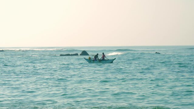 Fishermen sail boat among light ocean waves in summer evening. Men bail out water entered boat after colliding with wave slow motion