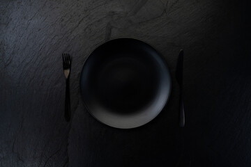 Minimalistic black plate with cutlery on dark background