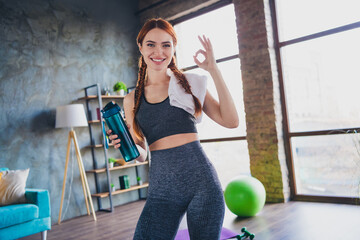 Photo of positive red hair girl sportswoman hold water bottle make okay sign in house indoors