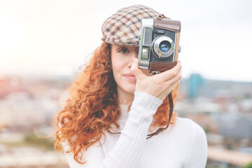 redhead lady taking pictures on vintage camera outside. Hobby and leisure concept toned image