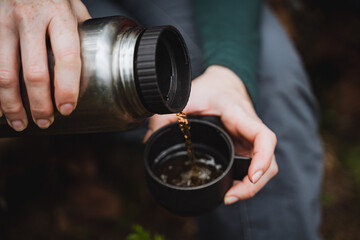 Hand holding camera lens pours coffee from thermos into cup