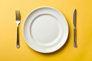 Top down view of a white plate isolated on yellow background with fork and knife with copy space.