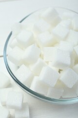 Many sugar cubes in glass bowl on white wooden table, closeup