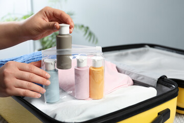 Woman with plastic bag of cosmetic travel kit packing suitcase, closeup