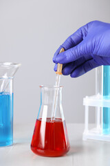 Scientist dripping liquid from pipette into flask at white table, closeup