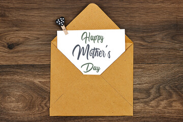 Mother's Day decorations concept. Top view photo of white invitation card with craft envelope  on wood table
