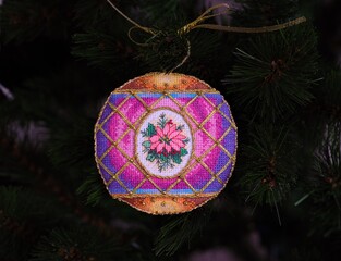 A cross stitched Christmas Timeless Elegance ornament on a Christmas tree. This Christmas ornament with poinsettia embroidered and made by myself.