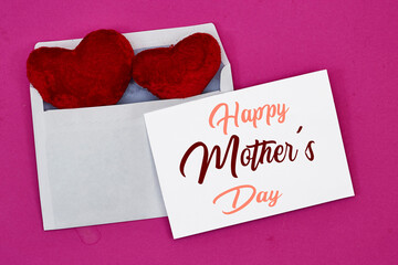 Mother's Day decorations concept. Top view photo of white invitation card with heart shape cushion toy on pink