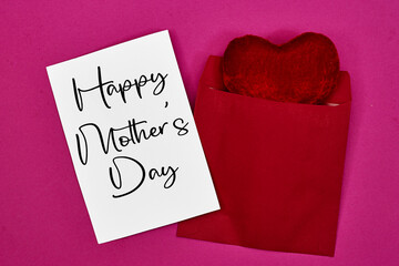 Mother's Day decorations concept. Top view photo of white invitation card with heart shape cushion toy on pink
