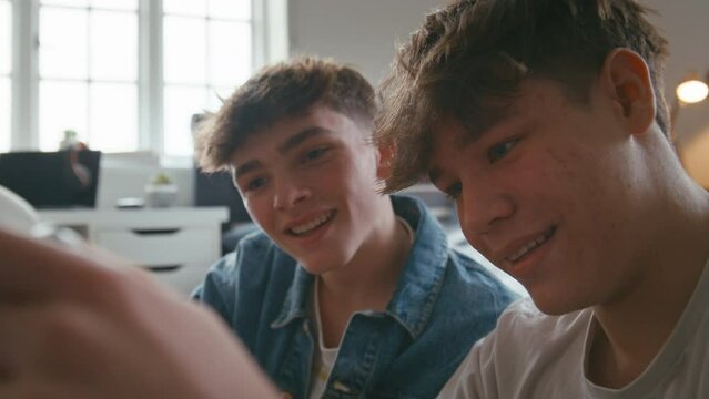 Close up of two teenage boys at home hanging out laughing playing with handheld computer gaming device in bedroom together  - shot in slow motion