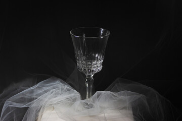 Copa de vidrio de vino vacío sobre un fondo oscuro, la copa está sobre un tul blanco, el tul es...