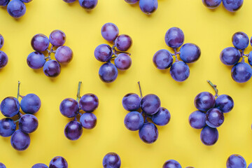 Fototapeta premium Fresh purple grapes on a vibrant yellow background, top view arrangement of juicy fruits