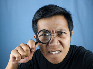 Funny Expression asian man looking through magnifying glass, searching or investigating something