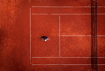Top view of woman playing recreational tennis on a clay court during the day.