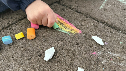 A child draws with chalk on the street. A rainbow pattern is drawn with multi-colored chalk on the asphalt on a sunny summer day. Creative development of children.