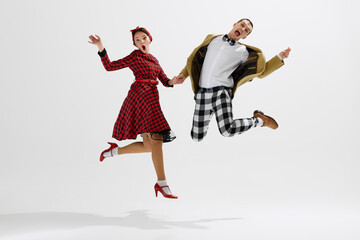 Man in checkered trousers and mustard jacket dancing with woman in red plaid dress playfully...