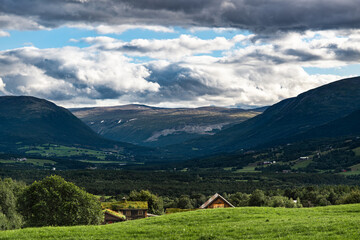 Obraz premium Evening falls over the serene Oppdal Valley in Norway, the farm roofs peaking just above the hillside and leading you further into the scene with mountains embracing the landscape
