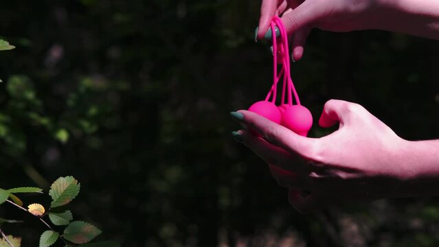 Woman's hand holds pink Kegel balls, Ben Wa balls against a background of green bushes in the forest. Vaginal balls in a woman's hand. Sex toys Geisha balls. Sex shop
