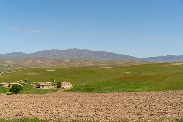 A large, empty field with a house in the distance. The sky is clear and blue