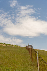 Obraz premium A fence is on a hillside with a clear blue sky. The fence is old and rusted