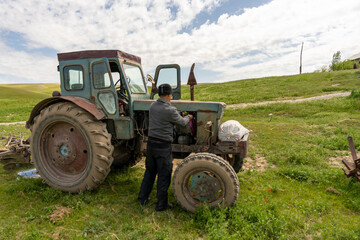 A man is working on an old tractor in a field. The tractor is old and rusty, and the man is trying to fix it. The scene is peaceful and quiet, with the man focused on his task