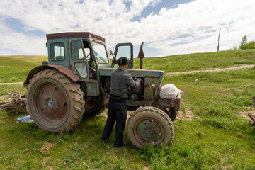 A man is working on an old tractor in a field. The tractor is old and rusty, and the man is trying to fix it. The scene has a nostalgic and somewhat melancholic mood