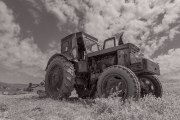 An old tractor is sitting in a field. The tractor is old and rusty, and it is surrounded by grass....