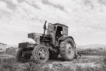 An old tractor is sitting in a field. The sky is cloudy and the tractor is covered in dirt