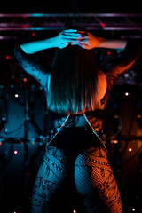 Portrait of a beautiful go-go dancer posing in a nightclub wearing black lace stockings. Blue...