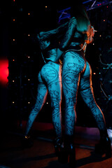 Portrait of two beautiful go-go dancers posing in a nightclub in black lace stockings. Blue...